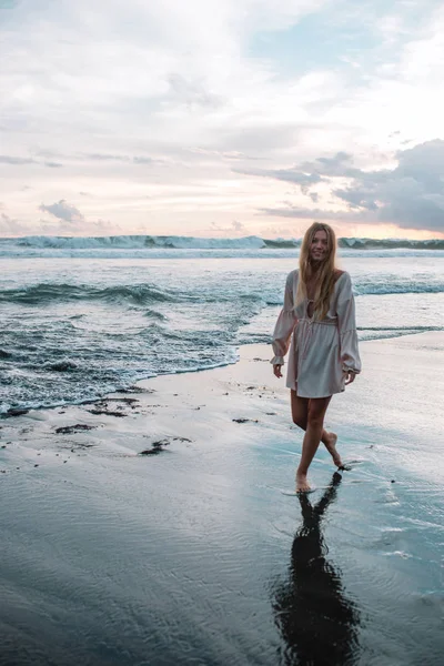 Chica rubia de pelo en un vestido rosa en la playa durante la puesta del sol, Indonesia, Bali — Foto de Stock