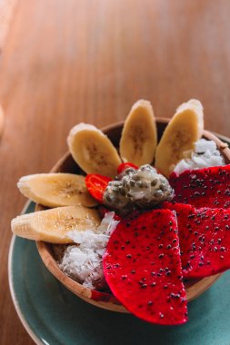 Muz, dragonfruit ve Hindistan cevizi ile güler yüzlü kase ahşap masa üzerinde pul