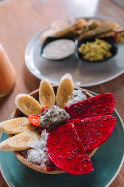 Muz, dragonfruit ve Hindistan cevizi ile güler yüzlü kase ahşap masa üzerinde pul