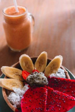 Muz, dragonfruit ve Hindistan cevizi ile güler yüzlü kase ahşap masa üzerinde pul