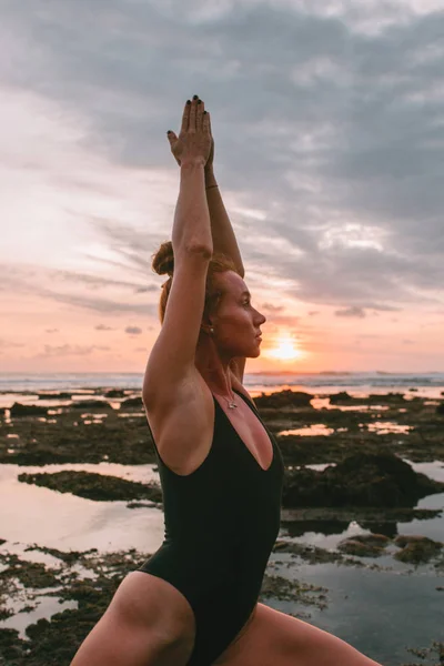 Joven chica atractiva practicando yoga en la playa durante el atardecer —  Fotos de Stock