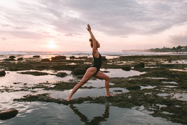 Молода приваблива дівчина практикує йогу на пляжі під час заходу сонця — стокове фото