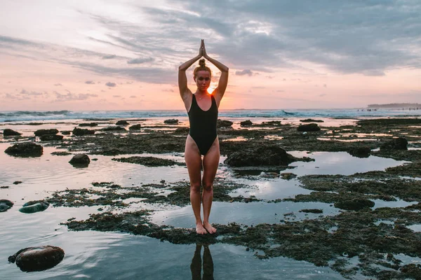 Menina atraente jovem praticando ioga na praia durante o pôr do sol — Fotografia de Stock