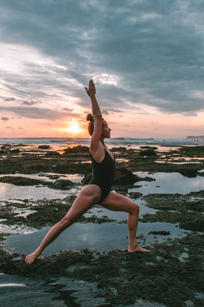 Menina atraente jovem praticando ioga na praia durante o pôr do sol — Fotografia de Stock