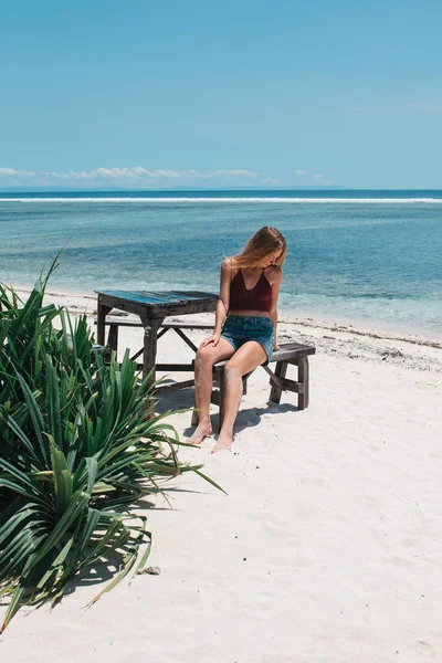 オーシャンビーチに木製のベンチに座っている若い美しい女性 ストック写真