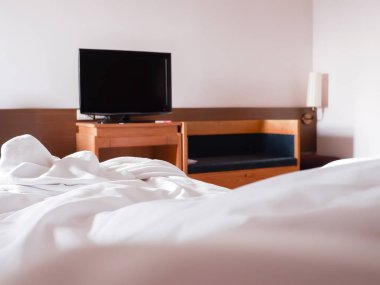 Beyaz buruşuk çarşaf ve dağınık yastıklar otel odasında.