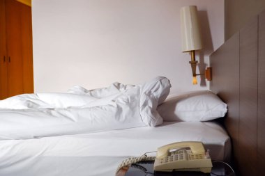 Otel odasında beyaz buruşuk çarşaflı ve dağınık yastıklı klasik telefon.