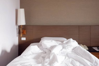 Beyaz buruşuk çarşaf ve dağınık yastıklar otel odasında.