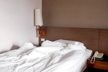 Beyaz buruşuk çarşaf ve dağınık yastıklar otel odasında.