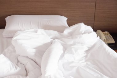 Beyaz buruşuk çarşaf ve dağınık yastıklar otel odasında.