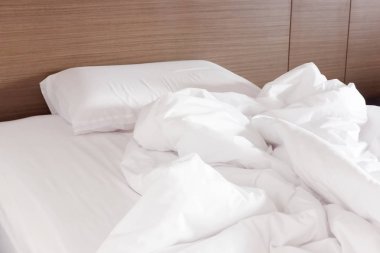 Beyaz buruşuk çarşaf ve dağınık yastıklar otel odasında.