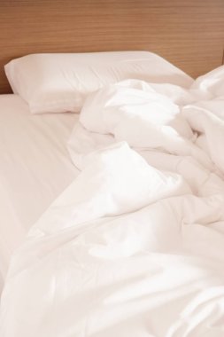 Beyaz buruşuk çarşaf ve dağınık yastıklar otel odasında.
