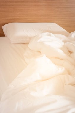 Beyaz buruşuk çarşaf ve dağınık yastıklar otel odasında.