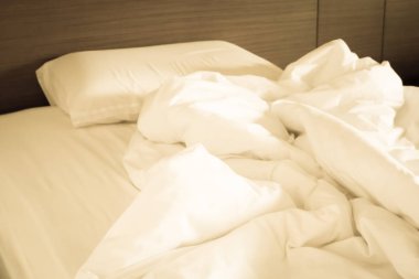 Beyaz buruşuk çarşaf ve dağınık yastıklar otel odasında.
