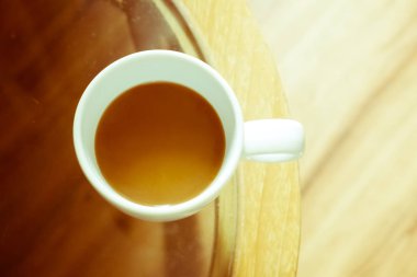 Bir fincan sıcak kahvenin üst görüntüsü. Oda lambasında cam masanın üzerinde duman var.