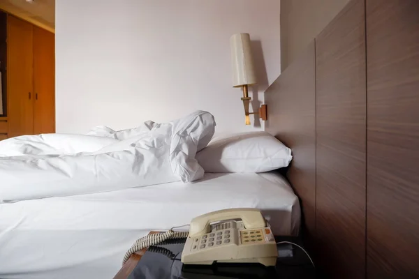 Vintage telephone with white crumpled bed sheet and messy pillows in a hotel room