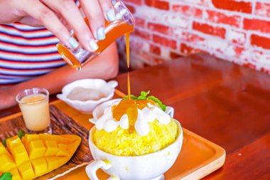 Kadın eli buz Bingsu 'nun üzerine mango şurubu döküyor (Kore tatlı tarzı) taze tatlı, mango meyvesi ve yapışkan pilavla birlikte.