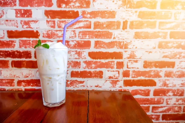 Iced milk with milk foam in tall glass on the wooden table and brick wall in cafe