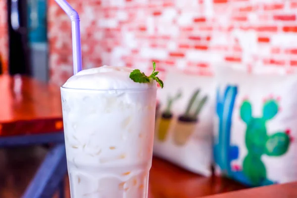 IJsmelk met melkschuim in hoog glas op de houten tafel en bakstenen muur in café — Stockfoto