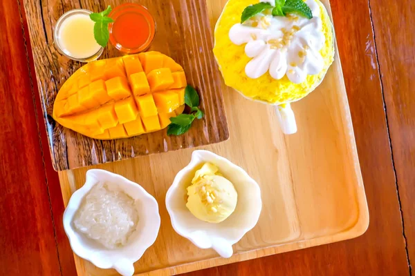 Bingsu (koreanischer Dessertstil) erfrischendes Dessert, serviert mit Mangofrüchten, Klebreis, Eis und gesüßter Kondensmilch auf dem Holzteller — Stockfoto