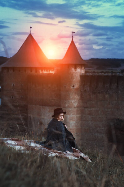 portrait of woman sitting on hill near castle at sunset