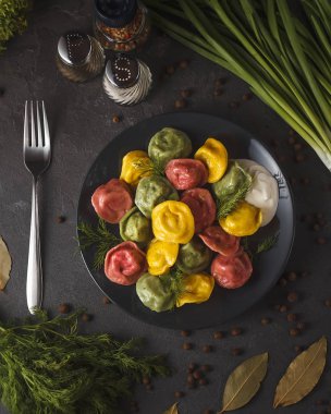 renkli tortellini üstten görünüm yeşillik ve baharat ile siyah plaka üzerinde