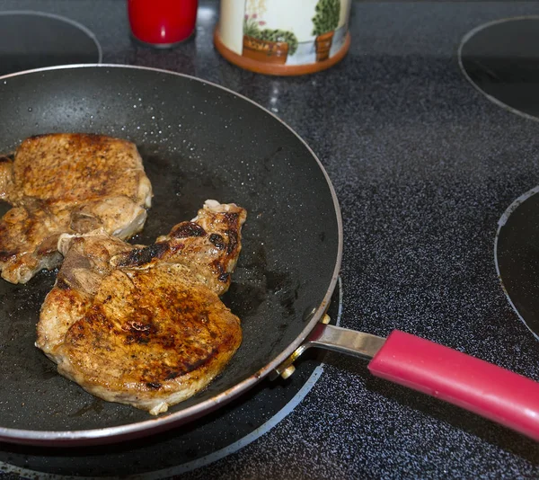 Sartén con chuletas de cerdo en la tapa de la estufa . — Foto de Stock