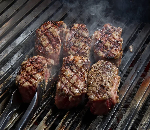 Steaks mit Gewürzen auf dem heißen Grill. Lebensmittel-Hintergrund. — Stockfoto