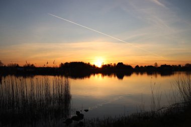 Güneş, Hollandsche IJssel nehrinin suyundan yükseliyor. Park Hitland 'daki hendeğin yanında.