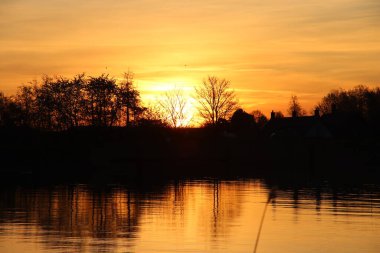 Güneş, Hollandsche IJssel nehrinin suyundan yükseliyor. Park Hitland 'daki hendeğin yanında.