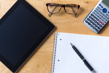 Tablet, gözlük, hesap makinesi ve not etmek üstünde ahşap çalışma masası