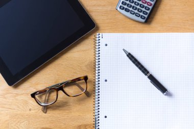 Tablet, gözlük, hesap makinesi ve not etmek üstünde ahşap çalışma masası