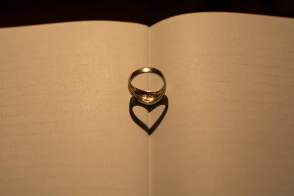 Un corazón hecho de la sombra de un anillo en un libro en blanco con línea — Foto de Stock