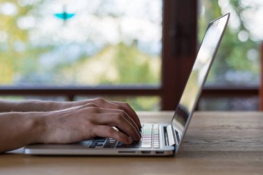 Ahşap masa üstünde pencere önünde dizüstü bilgisayarda yazarak