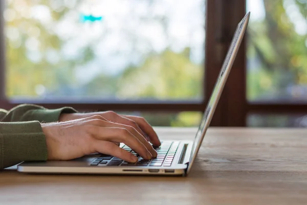 Ahşap masa üstünde pencere önünde dizüstü bilgisayarda yazarak