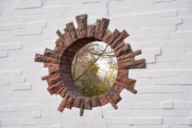 Parktaki tuğla duvardaki yuvarlak bir delik başka bir boyuta açılan bir kapı gibi görünüyor.