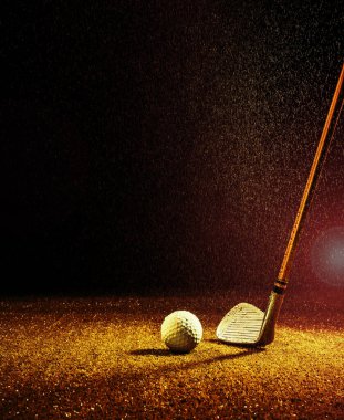 Yağmurdaki turuncu ışık demeti golf sopası ve golf topunu aydınlatıyor.