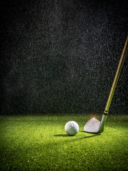 Beam of light in the rain illuminating a golf club and golf ball on the turf