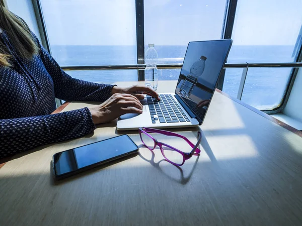 Woman using laptop computer, searching the web, browsing information while traveling on a ship to go on vacation