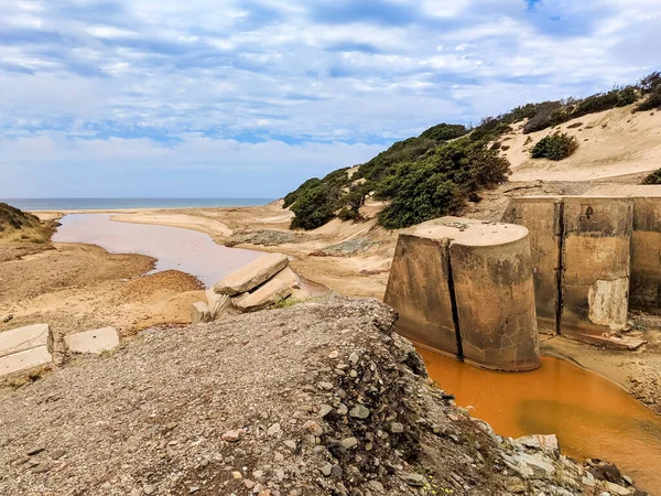 The Rio Piscinas crosses the dunes and invades the beach. Ruins on the Rio Piscinas which takes on a reddish color as it flows towards the sea and recalls the ancient mining activities of the Arbus area, Sardinia, Italy