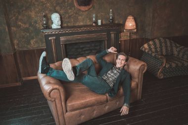 Şömine yakın bir deri kanepe üzerinde mutlu bir adam yatıyor