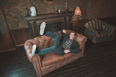 Şömine yakın bir deri kanepe üzerinde mutlu bir adam yatıyor