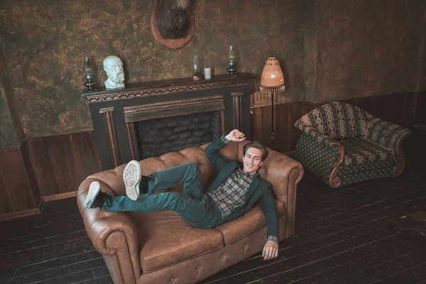 Um homem feliz jaz em um sofá de couro perto da lareira Fotografias De Stock Royalty-Free
