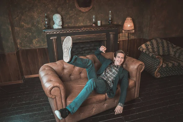 Um homem feliz jaz em um sofá de couro perto da lareira Fotografia De Stock