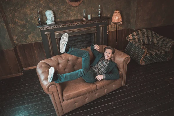 Um homem feliz jaz em um sofá de couro perto da lareira Imagem De Stock