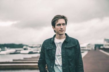 Kot pantolon giymiş bir adam bir Yat kulübünde bulutlu havalarda Nehri yakınında bir iskelede duran ve gülümseyen