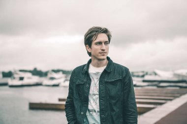 Kot pantolon giymiş bir adam bir Yat kulübünde bulutlu havalarda Nehri yakınında bir iskelede duran ve gülümseyen