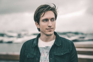 Kot pantolon giymiş bir adam bir Yat kulübünde bulutlu havalarda Nehri yakınında bir iskelede duran ve gülümseyen