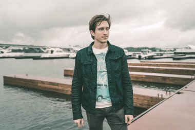 Kot pantolon giymiş bir adam bir Yat kulübünde bulutlu havalarda Nehri yakınında bir iskelede duran ve gülümseyen