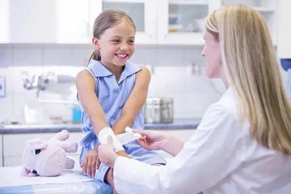 小学校低学年の女の子の腕に包帯を適用する看護師 — ストック写真